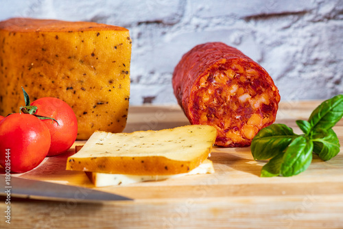 Sliced kulen and semi-hard cheese arranged neatly on a plate, garnished with fresh basil leaves. The vibrant colors of the red cured sausage, creamy-yellow cheese, and green basil create a visually ap