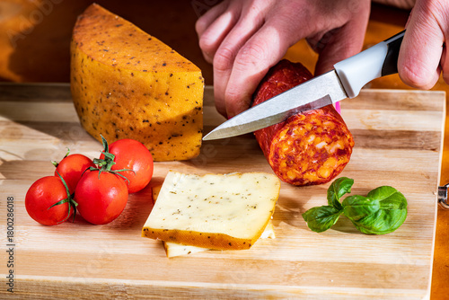 Sliced kulen and semi-hard cheese arranged neatly on a plate, garnished with fresh basil leaves. The vibrant colors of the red cured sausage, creamy-yellow cheese, and green basil create a visually ap