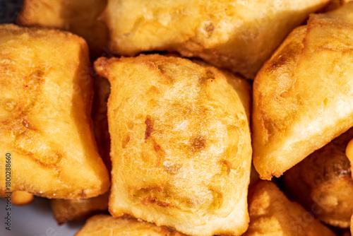 Golden, freshly fried fritters arranged on a plate, featuring a crispy exterior and a soft, airy inside. Warm lighting enhances their rich golden color and homemade rustic appearance.