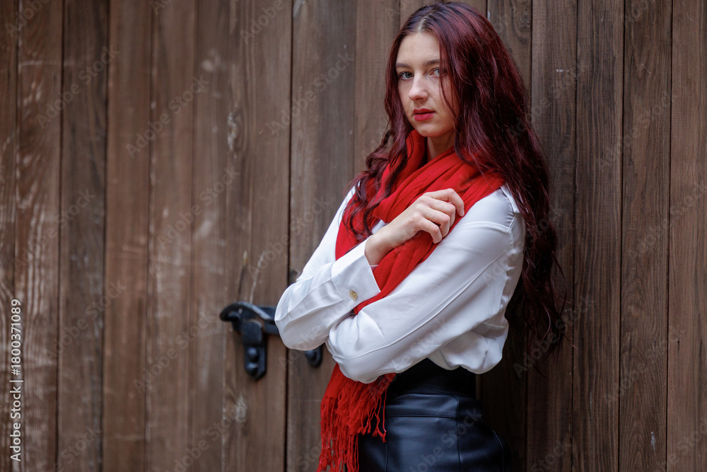Fototapeta premium Young woman posing in front of wooden door with red scarf