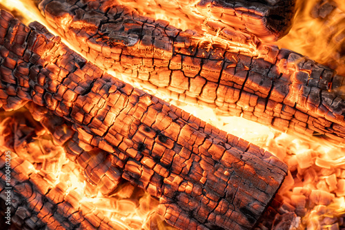 Charred wooden logs glowing in a warm fire, showcasing intricate textures and vibrant orange flames, creating a cozy and inviting atmosphere for outdoor gatherings