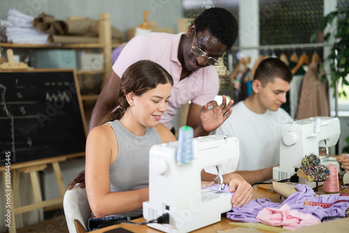 Obraz na plátně Polite middle-aged man instructor controlling students using sewing-machine at d