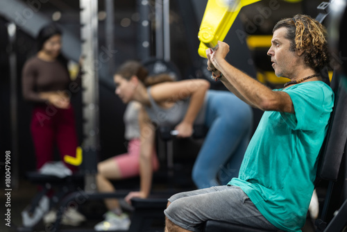 Photos Adult man doing strength exercises on his shoulders while sitting in a press machine