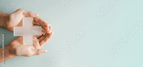 Hands holding Plus cross model on blue background, medical healthcare, wellness support, positivity concept
