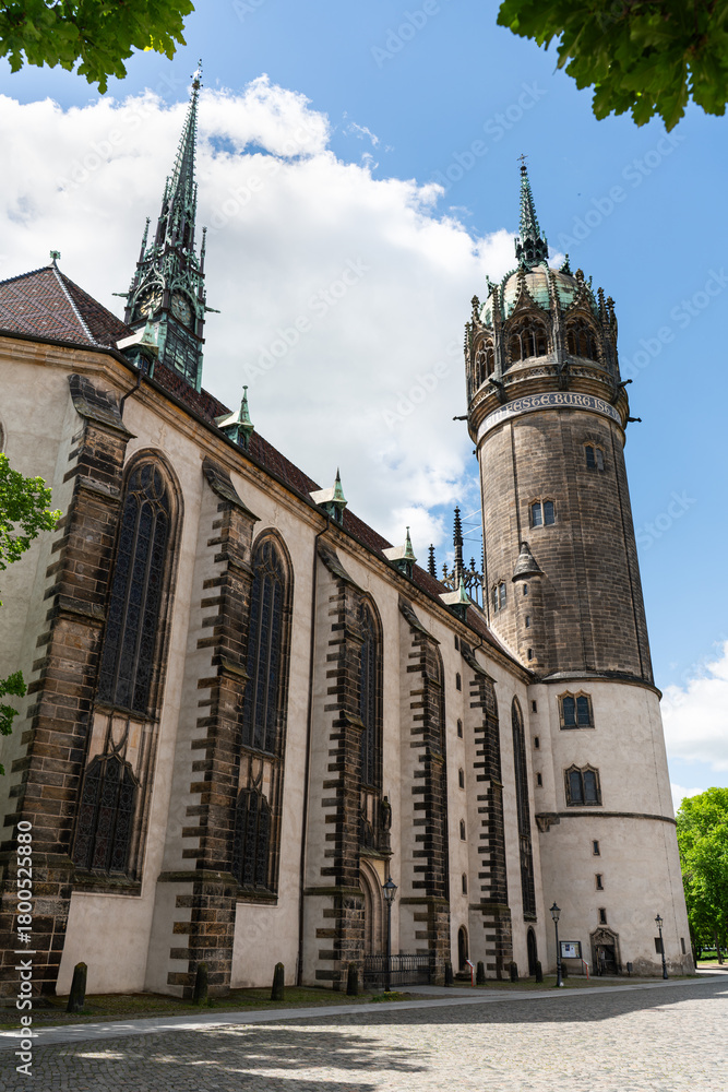 Obraz premium Side view of the Castle Church in Wittenberg, framed by leaves. Historic site where Martin Luther posted the 95 Theses.