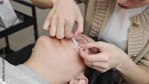 A cosmetologist's girl glues a patch onto the client's eyelid.