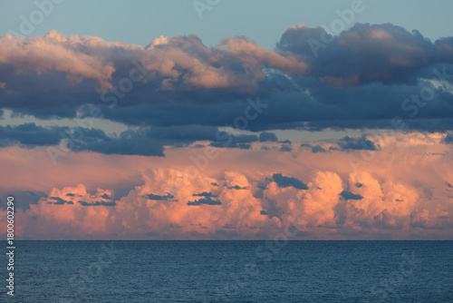 Dramatic sunset clouds glowing in warm light above a calm Mediterranean sea, with layered storm clouds and soft pastel tones.