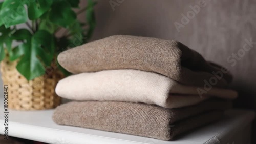 Three cashmere sweaters are folded on a white wardrobe with a flower.