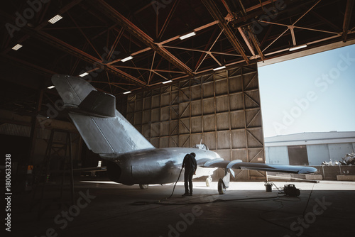 A silhouetted man paints a vintage jet inside a military hanger