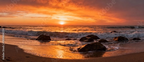 Sunset over a rocky beach with waves crashing onto the shore, casting golden reflections on wet sand.