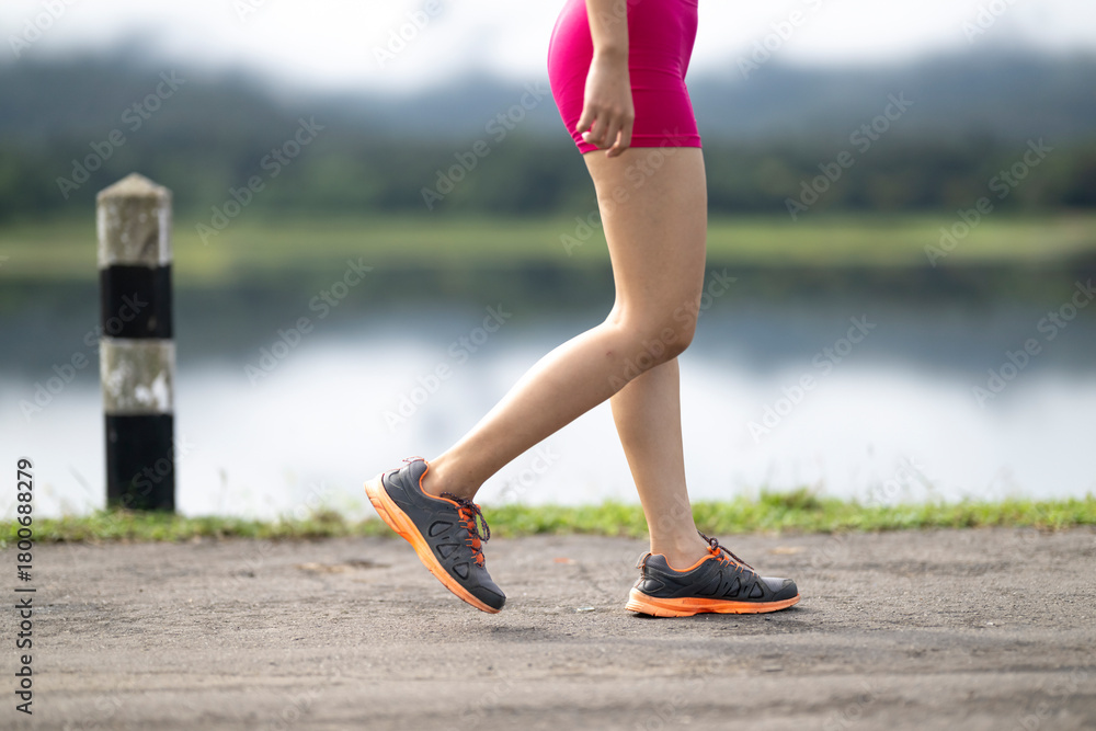 Fototapeta premium Woman exercising outdoors walking with running shoes by lake