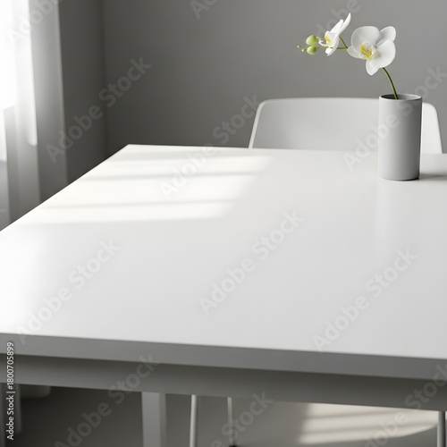 Minimalist white table with a simple white vase holding a delicate orchid flower in a modern, bright room setting