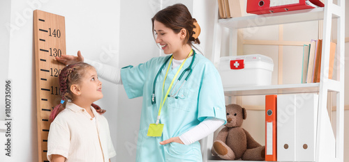 Female pediatrician measuring little girl's height near stadiometer in clinic