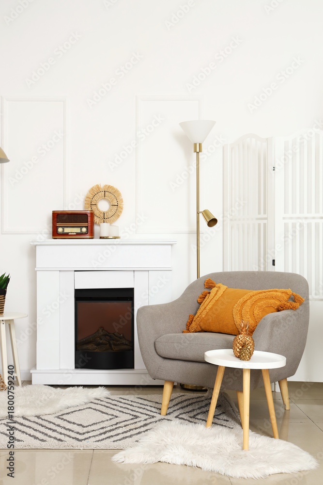 Naklejka premium Cozy grey armchair with cushion, fireplace and coffee table in interior of living room