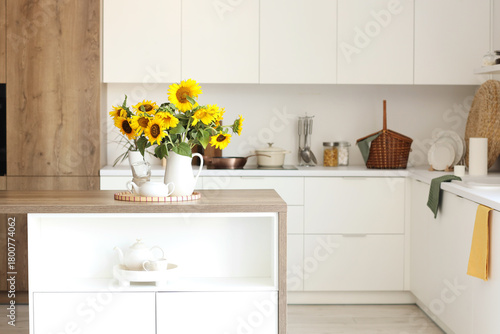 Vase with sunflowers, teapot and cups on dining table in light kitchen