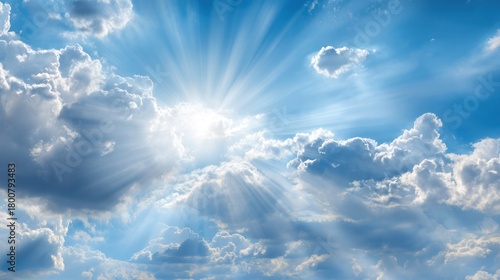 Fototapeta Naklejka Na Ścianę i Meble -  A bright blue sky with white clouds and a sun shining through, casting rays of light across the scene.