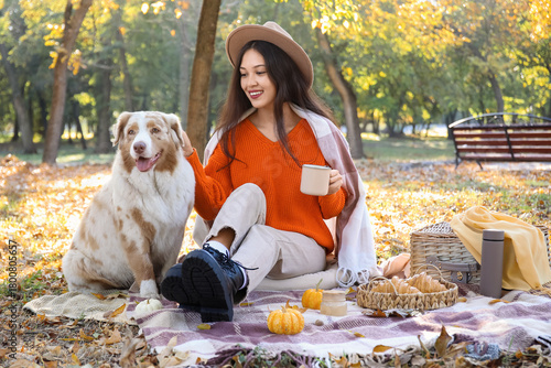 Young happy Asian woman with cups of tea, croissants and Australian Shepherd ...