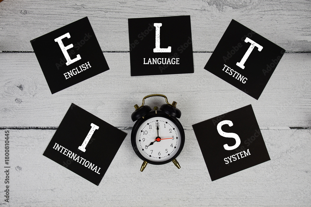 Obraz premium IELTS International English Language Testing System with alarm clock on wooden background