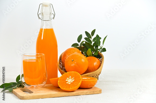 Freshly squeezed orange juice in a glass, a full bottle, and an arrangement of whole and sliced oranges against a white background.