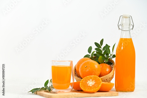 Freshly squeezed orange juice in a glass, a full bottle, and an arrangement of whole and sliced oranges against a white background.