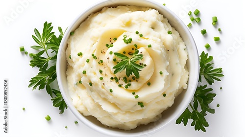 A bowl of creamy mashed potatoes garnished with herbs on a white surface view from above
