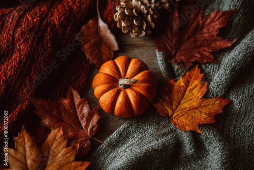 Cozy autumn still life with small pumpkin, pine cone, dry leaves, and knitted sweaters backgound. Warm Thanksgiving composition, rustic fall decor for seasonal comfort and home