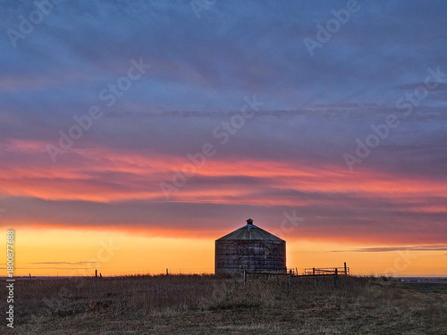 Amazing and dramatic prairie sunrise with blue, pink, yellow and orange colors with a granary in silhouette.