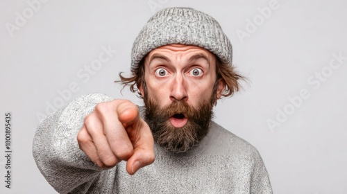 Surprised bearded man in beanie pointing at camera with shocked expression