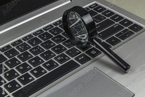 Magnifying glass placed on a laptop keyboard in an office setting