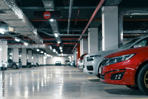 Row of parked cars in a modern underground parking garage with bright ceiling lights and clean concrete floor. Urban infrastructure interior suitable for themes of real estate, security, transportatio