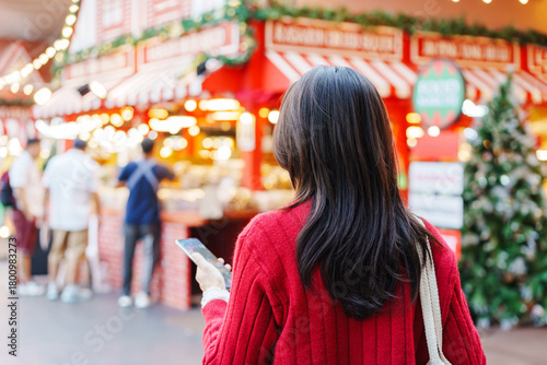 Young Asian woman wearing red cardigan and using smart phone at Christmas market