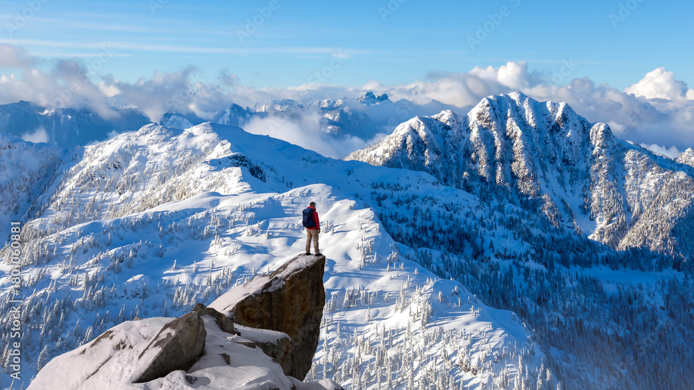 Fototapeta premium Winter Mountain Climber Standing on Snow-Covered Peak Overlooking Vast Icebound Range Under Clear Blue Sky