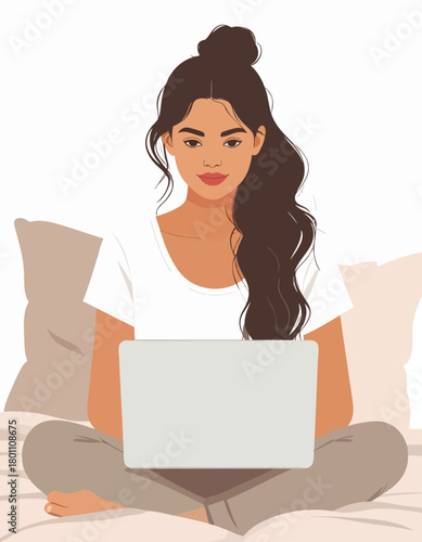 Woman sitting cross-legged on a bed, using a laptop. She is wearing casual clothes and has her hair up.
