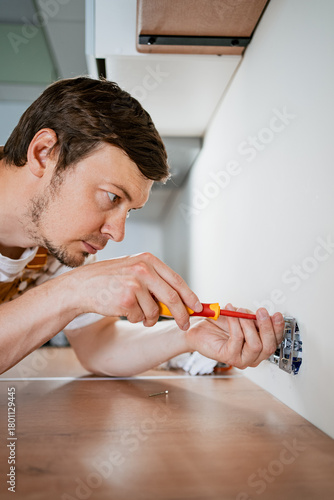 Focused electrician carefully installs electrical sockets in a contemporary kitchen, utilizing a screwdriver with precision and expertise during a home renovation project