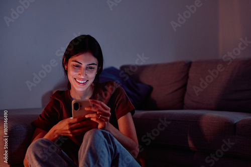 Canvas Print Young woman relaxing at home, enjoying content on her mobile phone, with the scr