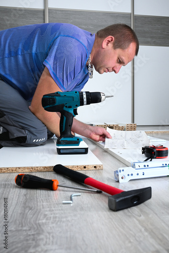 Wallpaper Mural Person kneeling on floor assembling furniture, reading instructions with tools provided Torontodigital.ca