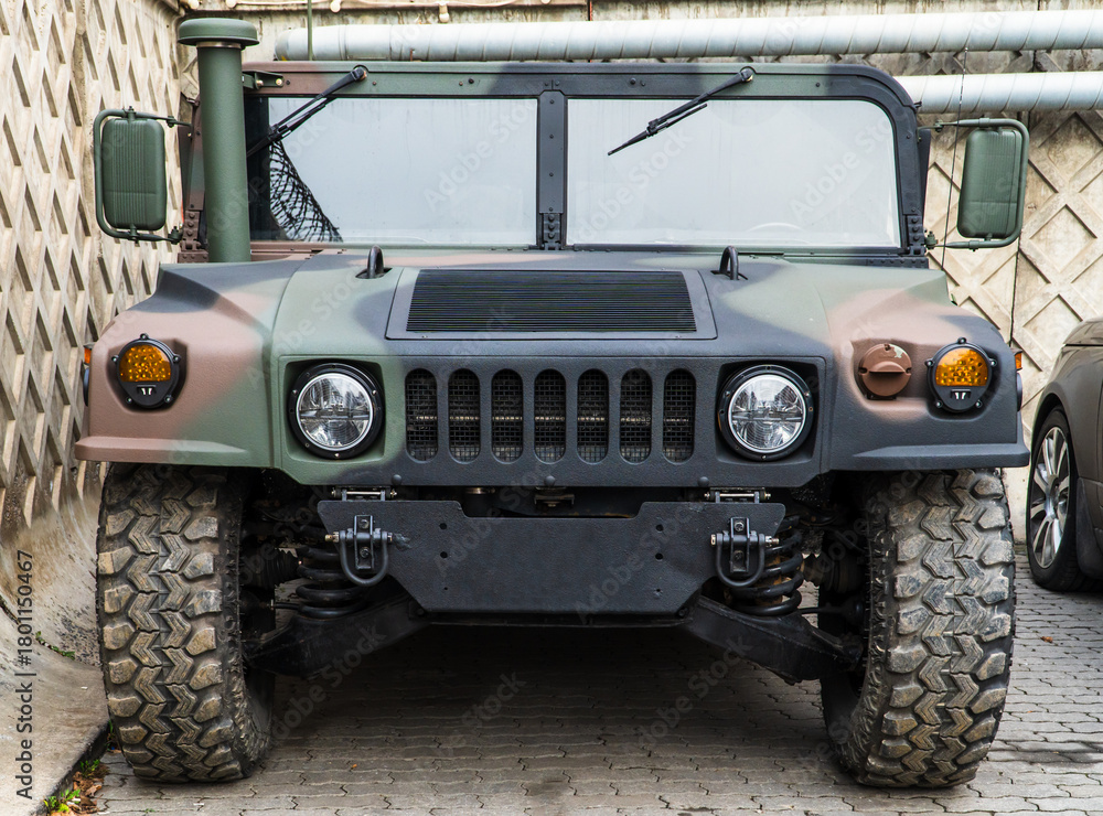 Naklejka premium Military Humvee parked on an street, showcasing its rugged design and operational readiness in a secure military base. Khaki camouflage military Hummer front view. Army USA.