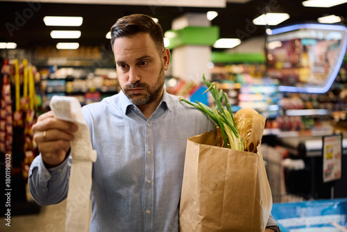Tableau sur toile Worried man checking the bill after buying groceries at supermarket
