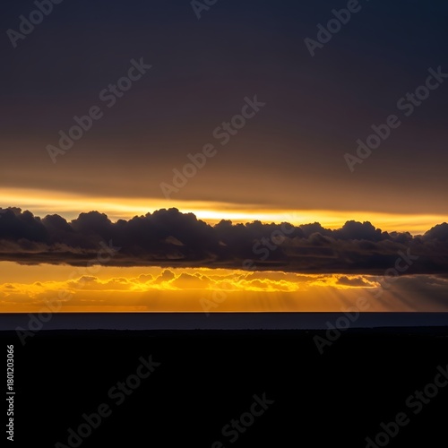 A stunning sunset over the ocean with vibrant golden and orange hues illuminating the sky and dark clouds creating a dramatic atmosphere