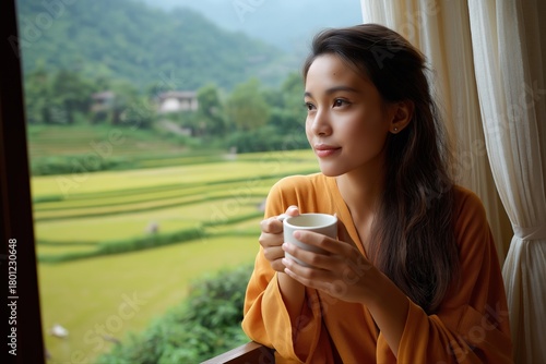 Young asian woman enjoying coffee with scenic view of lush landscapes from window