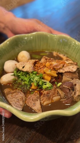 vertical video of Thai boat noodle bowl with rich broth meat slices herbs and steamed balls
