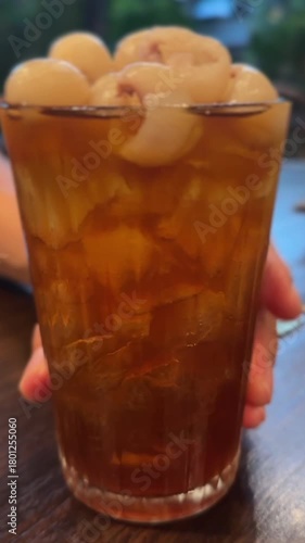vertical video of fresh longan juice in tall glass with ice and whole longans on top
