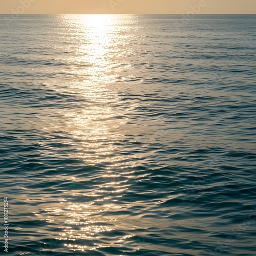A serene view of the ocean with gentle waves reflecting sunlight during sunset, creating a peaceful and calming atmosphere over the water surface