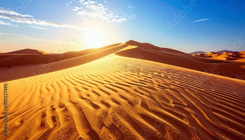 Fototapeta Naklejka Na Ścianę i Meble -  Vast desert landscape with undulating sand dunes, illuminated by the warm glow of the sun, under a clear blue sky.