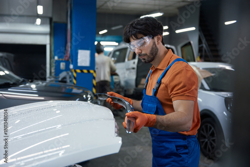 Auto body technician repairing car hood in professional garage workshop with safety gear