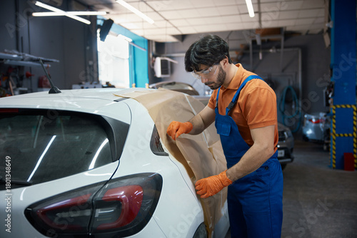Automotive technician prepping compact car in garage for paint and bodywork refinishing