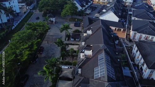 Beautiful aerial of photovoltaic solar panels on the rooftops of modern houses in a luxury neighborhood in Abuja, Nigeria. A man walk around the house towards the entrance gate.