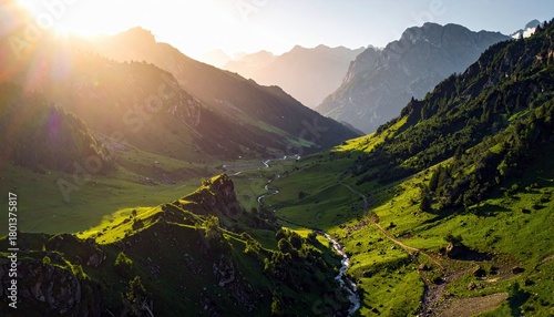A breathtaking mountain valley bathed in the warm glow of golden hour sunlight, featuring rolling green hills, a winding river, and majestic, rugged peaks.