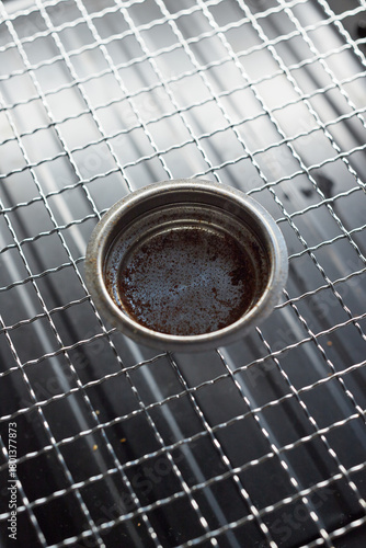 Close-up of dirty portafilter on metal grate.