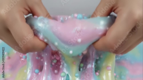 Close-up of hands playing with colorful pastel slime. Squeezing and stretching a gooey, textured substance with beads. ASMR and satisfying sensory video concept